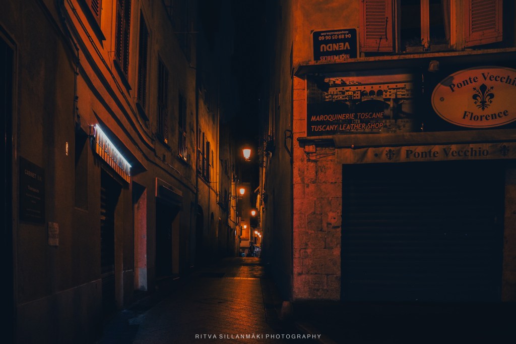 A dimly lit street in Nice, highlighting warm streetlights and a mysterious vibe.