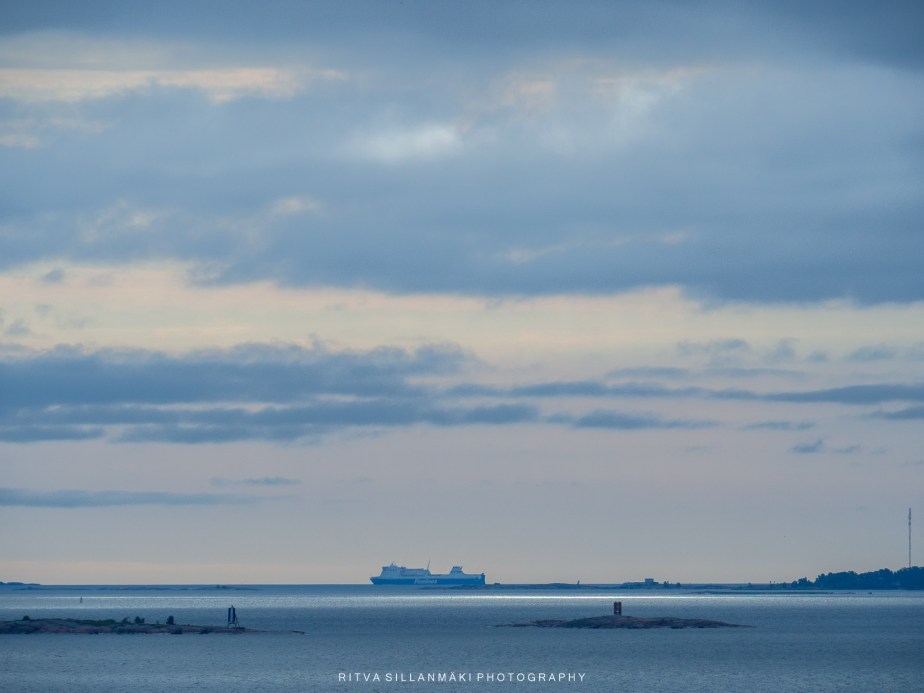 A ferry cruises across calm blue waters beneath layered clouds