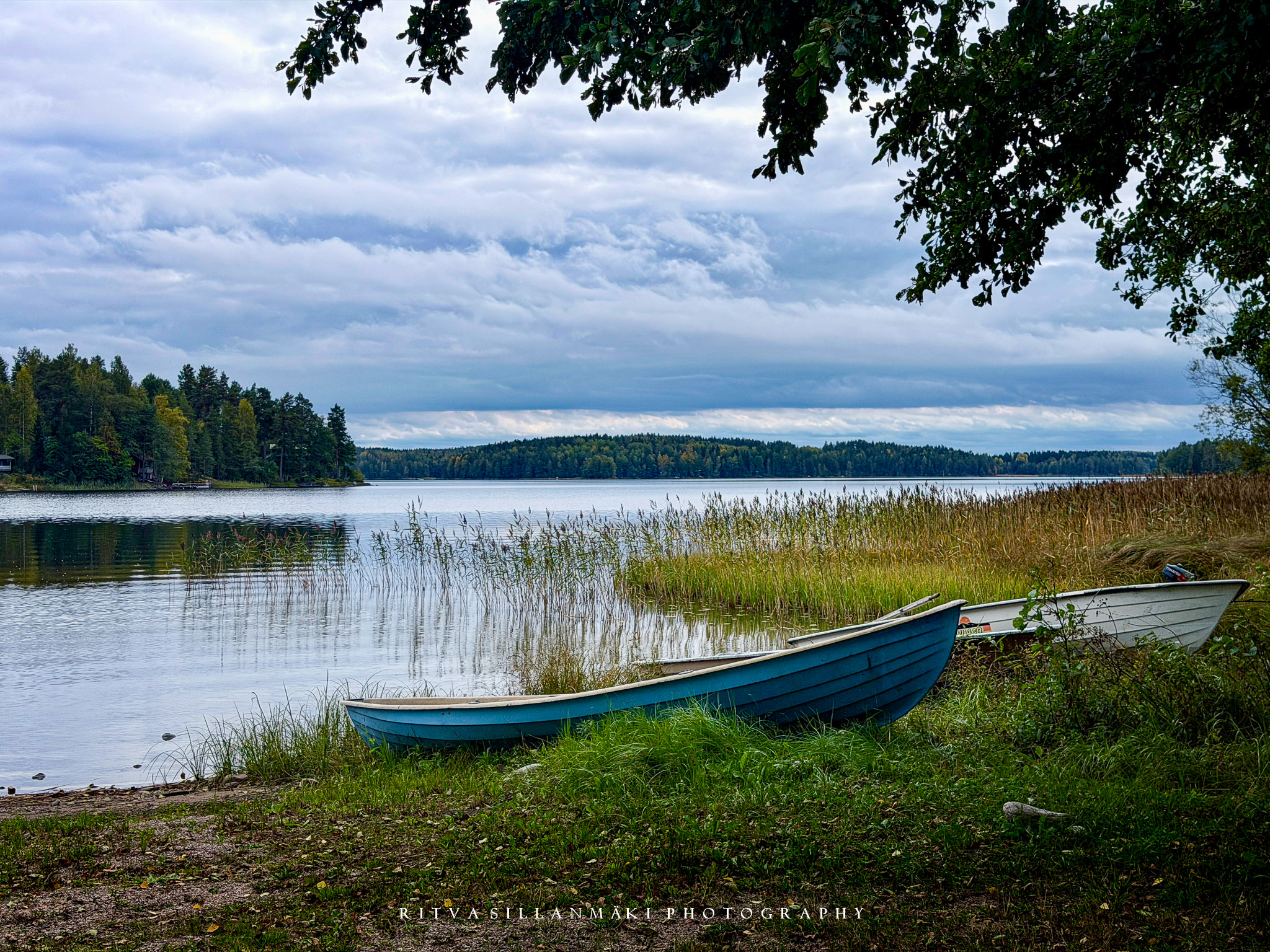 Two boats rest along a peaceful forest-lined lake beneath a dramatic, cloud-filled sky.